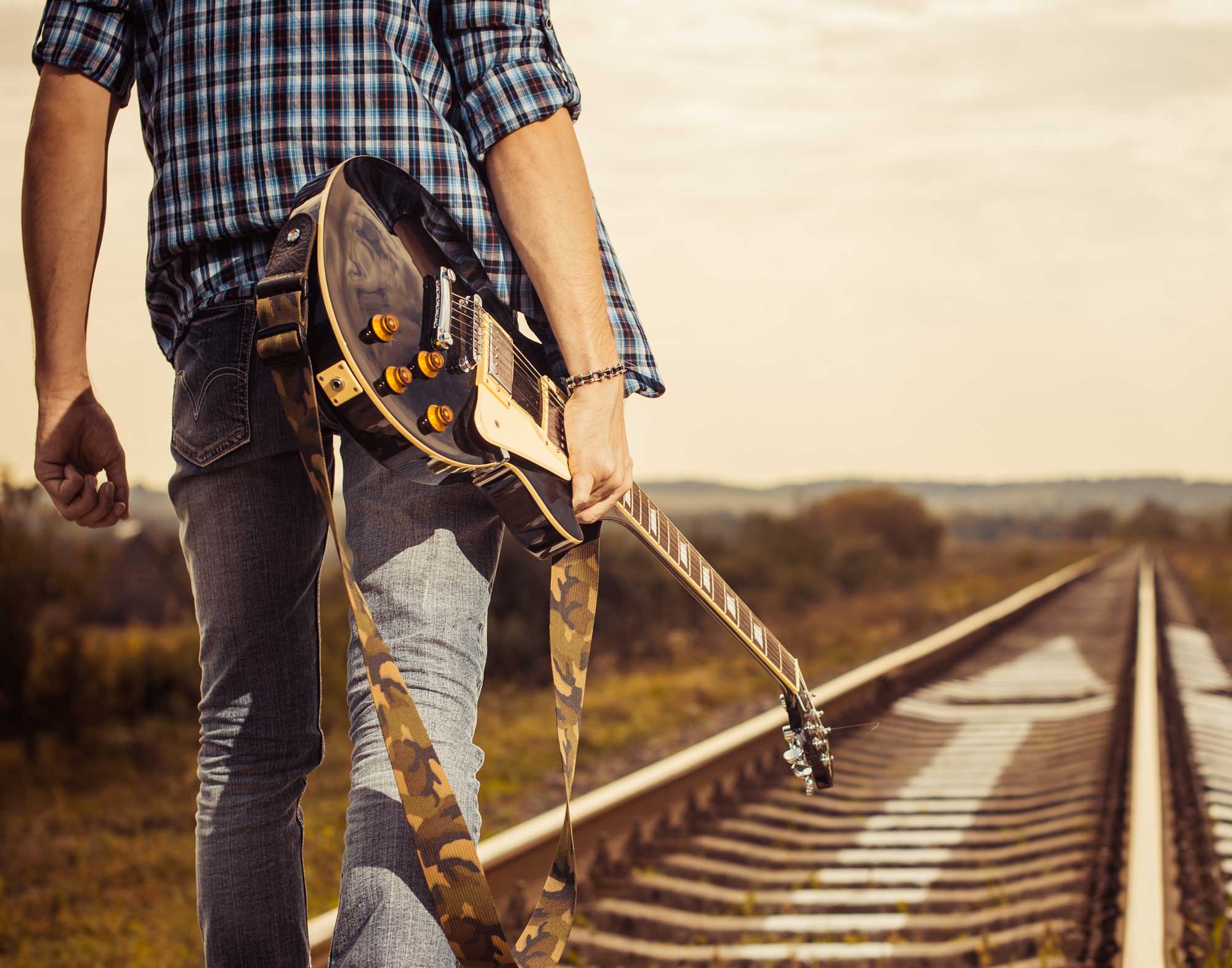 man walking down railroad track with guitar